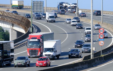 Trafic intens de autoturisme, camionete și camioane în deplasare pe un nod rutier supraetajat al unei autostrăzi.