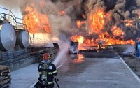 În curtea unei hale industriale, un pompier echipant cu aparat de respirat stă în genunchi pe o platformă betonată și direcționează un jet de apă spre un incendiu violent, sutești, valcea, 3 octombrie 2026