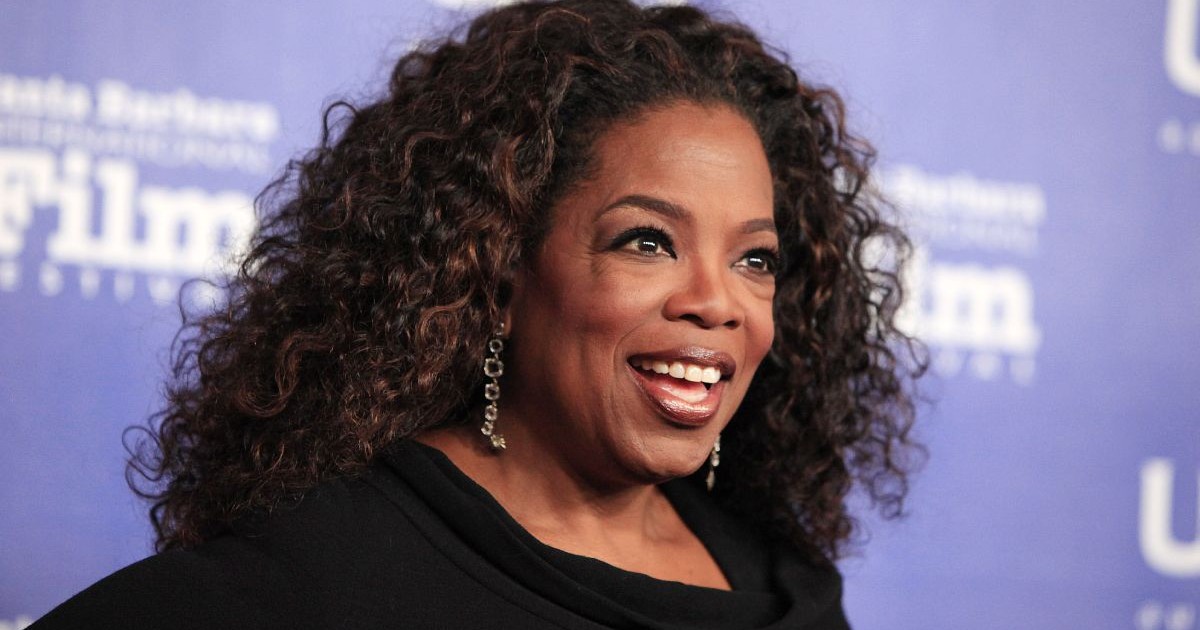 Oprah Winfrey, îmbrăcată cu o bluză neagră, pe fundal albastru