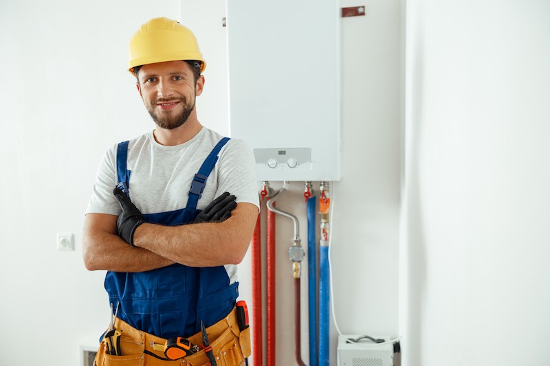 Smiling technician servicing the house heating system looking at camera while standing with arms crossed. Installation and setting the new gas boiler for hot water and heating