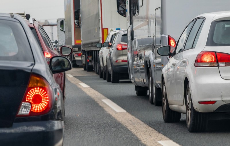 O coloană aglomerată de autoturisme și vehicule mari de marfă prinse într-un ambuteiaj pe mai multe benzi ale unei șosele.