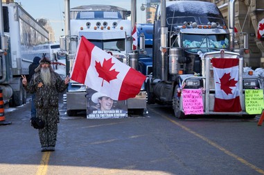 Un protestatar, cu steagul Canadei în mână, în fața camioanelor care blochează centrul Ottawa | Foto: EPA