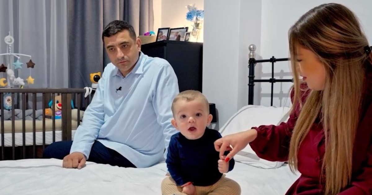 George Simion, îmbrăcat cu o cămașă, în timp ce stă pe pat, alături de fiul său, Radu, și de soția sa, Ilinca, îmbrăcată într-o rochie roșie