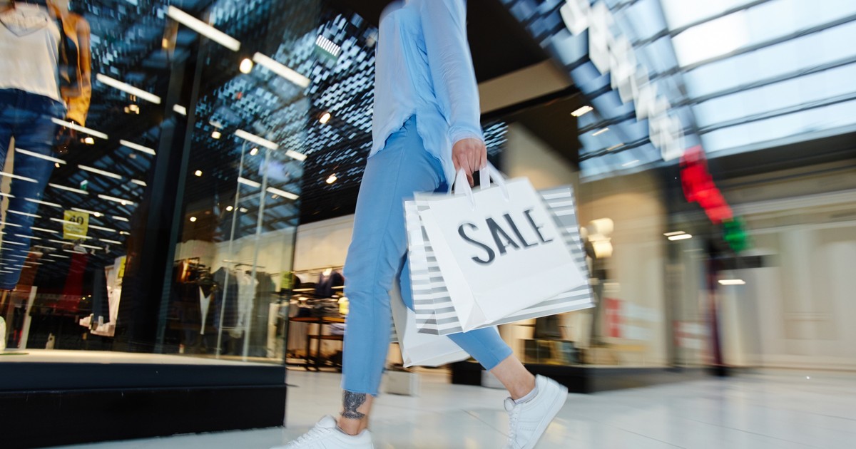Care este momentul potrivit al anului să cumperi diferite lucruri - Imagine cu o tânără care iese dintr-um magazin cu mai multe plase în mână.