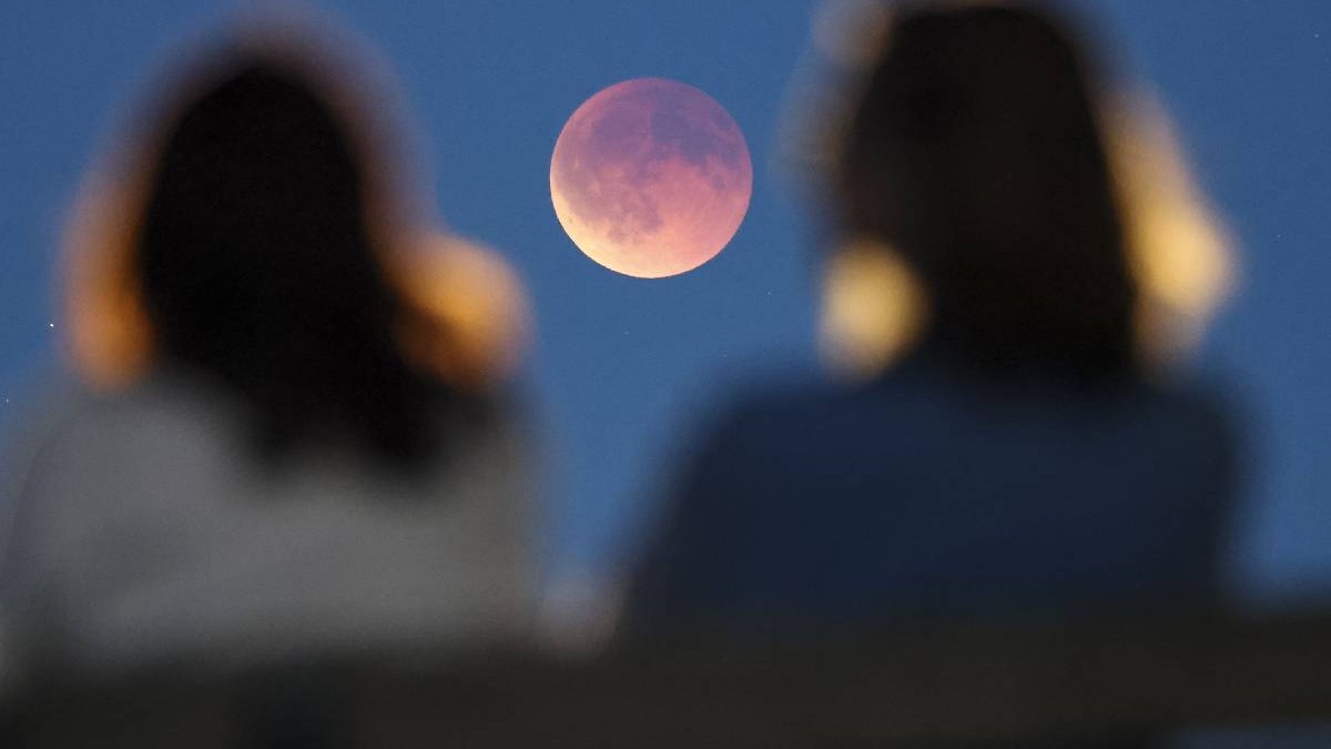 două femei privesc Luna, satelitul natural al Pământului în timpul unui eveniment astronomic