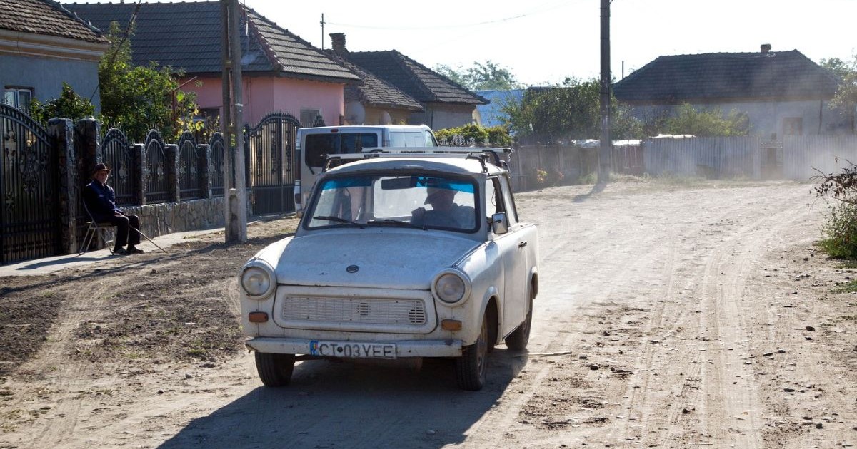 Trabant vechi, de culoare deschisă, pe o stradă neasfaltată, în timp ce scoate fum, în satul Piscu Vechi din județul Dolj