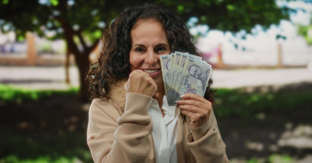 O femeie de vârstă mijlocie ține cu entuziasm în mână mai multe bancnote românești de 100 de lei, într-un parc, sugerând succes financiar