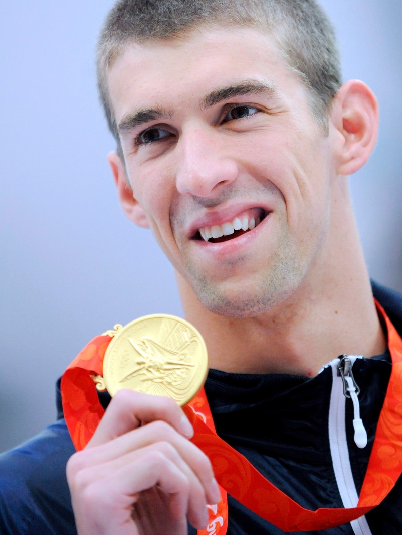 epa01443029 US swimmer Michael Phelps shows his gold medal from the mens 200m butterfly final at the 2008 Olympics at the National Aquatic Center in Beijing, China, 13 August 2008. The historic swimming gold takes Phelps to a world all time mens record of 10 gold medals breaking the world record of nine career golds and putting him at halfway mark of four golds to reach his target of another world record of eight gold's at a single Olympics currently held by Mark Spitz. EPA/KAY NIETFELD