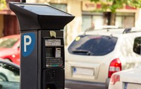 Prim-plan cu un aparat electronic de plată a parcării, alimentat cu panou solar, amplasat pe marginea unei străzi cu mașini parcate.
