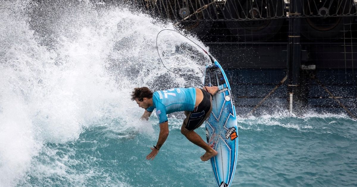 Australianul Jack Robinson concurează în timpul turneului Surf Abu Dhabi Pro, pe 16 februarie 2025. In imagine, sportivul in tricou bleu si sort negru, este pe placa de surf albastra
