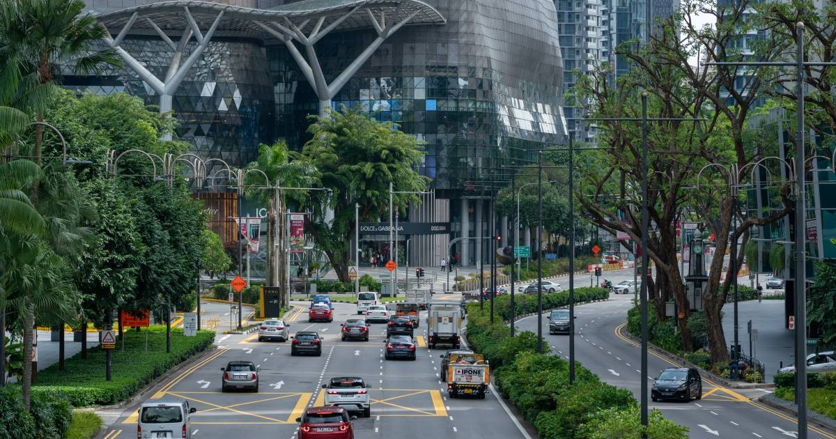 mai multe masini aflate pe o sosea cu 5 benzi pe sens in singapore. se observa o cladire mare in fata