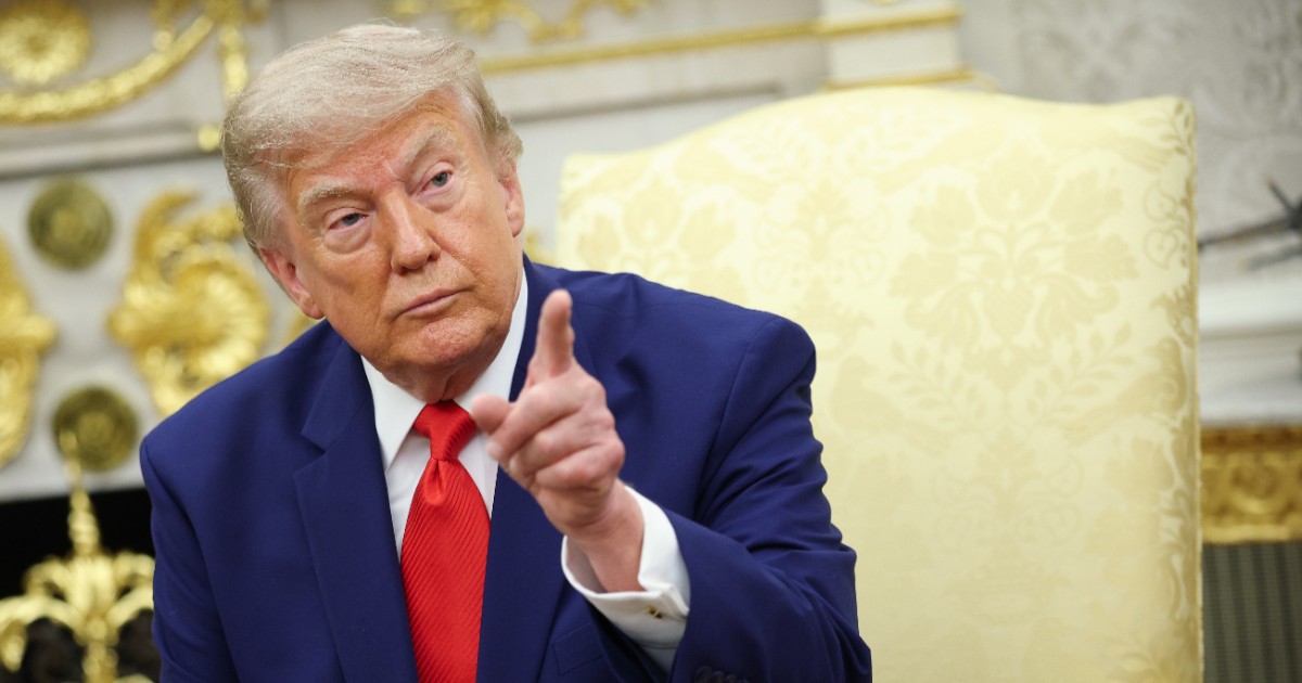 Președintele american Donald Trump, în timp ce stă pe fotoliu la Casa Albă, poartă un costum albastru și o cravată roșie și arată cu degetul spre cameră
