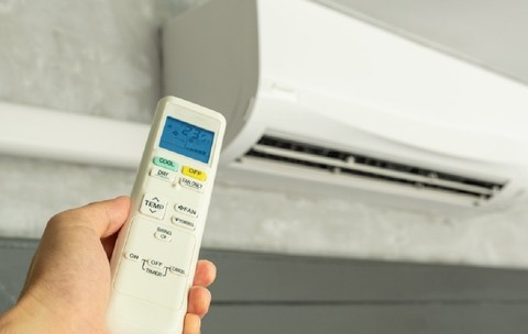 Imagine cu o mână de bărbat care ţine o televomandă în dreptul unui aparat de aer condiţionat