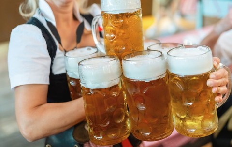 O chelneriță îmbrăcată în costum tradițional bavarez, ținând și transportând mai multe halbe de bere într-un cort de la Oktoberfest din München, Germania