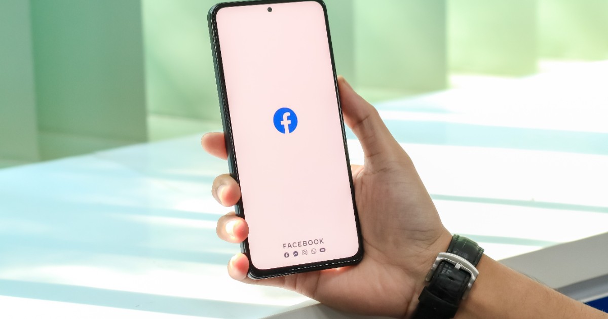 Un bărbat care ține un telefon în mână pe care accesează Facebook