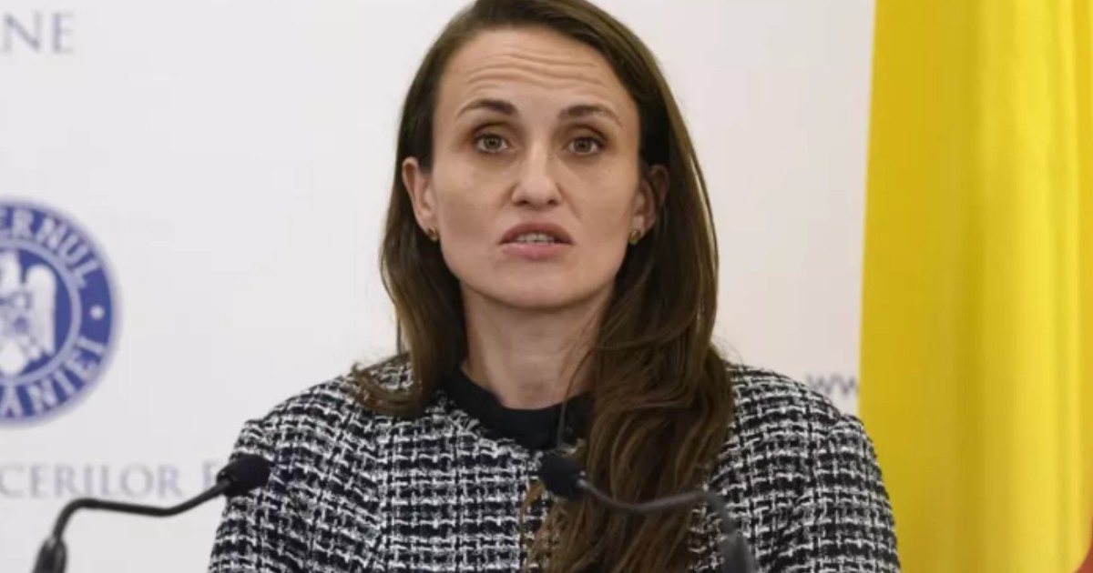 Oana Țoiu într-un sacou negru cu alb, în timp ce vorbește la microfon.