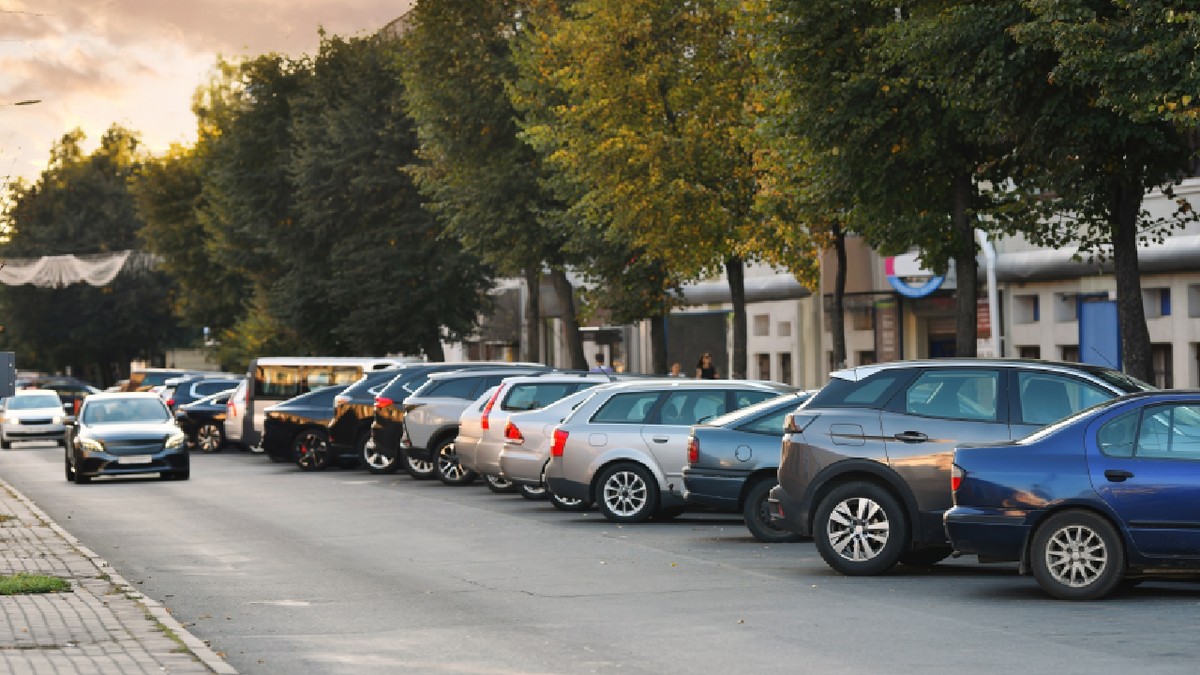 Rânduri de mașini parcate strâns de-a lungul drumului pe o stradă rezidențială îngustă