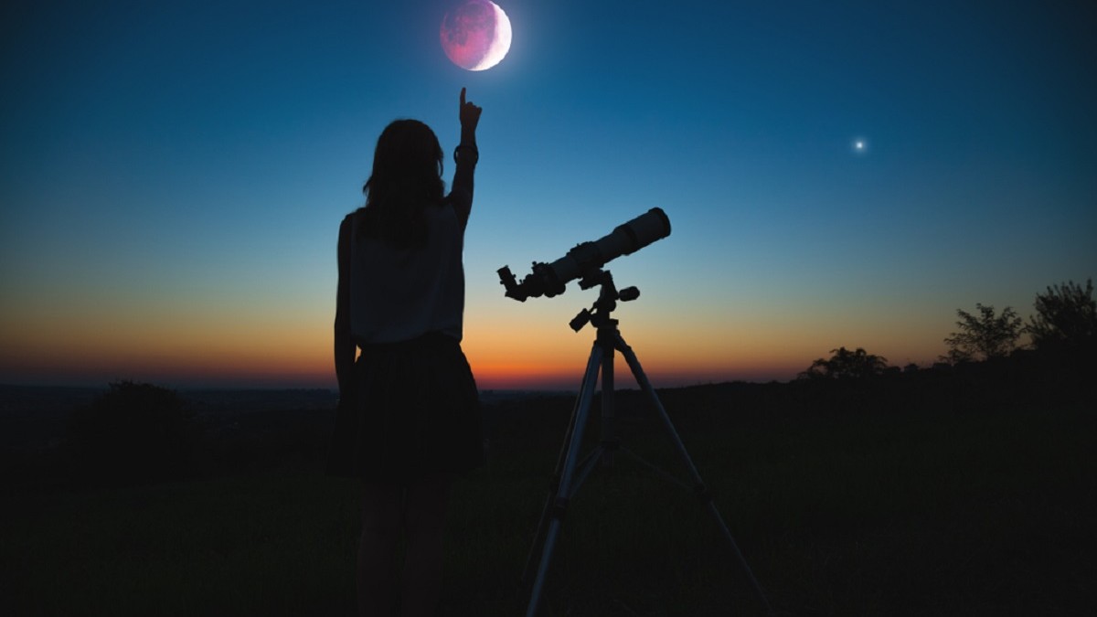 Eclipsa de Lună plină în Pești din 28 august 2026: ce aduce pentru fiecare zodie și cum ne afectează sănătatea - O siluetă de femeie care arată cu degetul spre o eclipsă de lună, lângă un telescop Sursa foto: Shutterstock