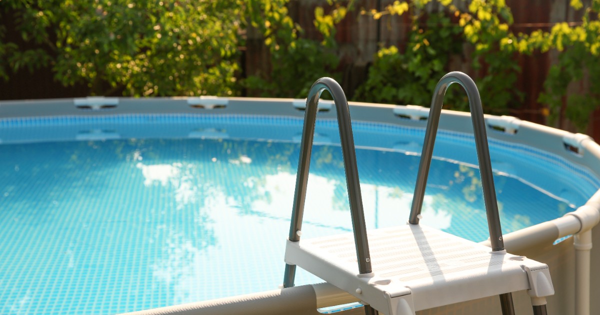 O piscina din plastic amplasată într-o curte, are o scara din plastic pe care te poți urca