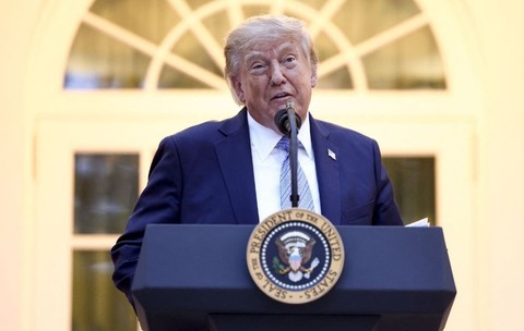 Donald Trump, îmbrăcat într-un sacou bleumarin, o cămașă albă și o cravată bleu, vorbind din spatele unui pupitru de lemn masiv dotat cu microfon, în cadrul unei cine organizate în Grădina Trandaf