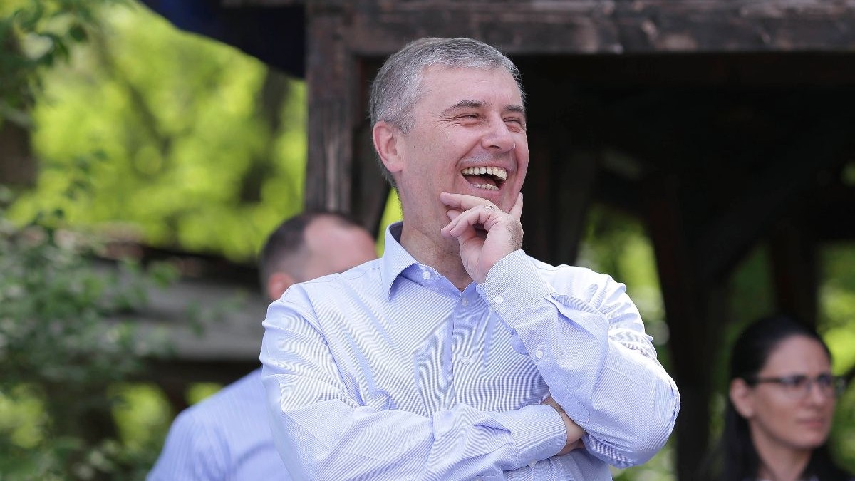 Lucian Pahonțu, în cămașă deschisă la culoare, râde cu mâna stângp sub bărbie