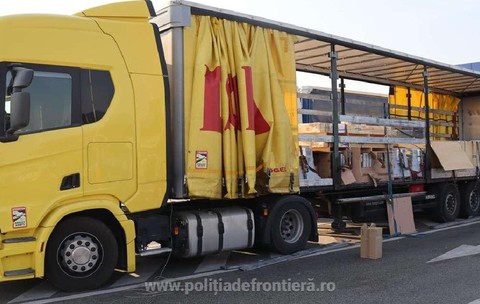 Un camion galben cu prelata de la remorca data la o parte, se vad mai multe cutii si paleti in remorca