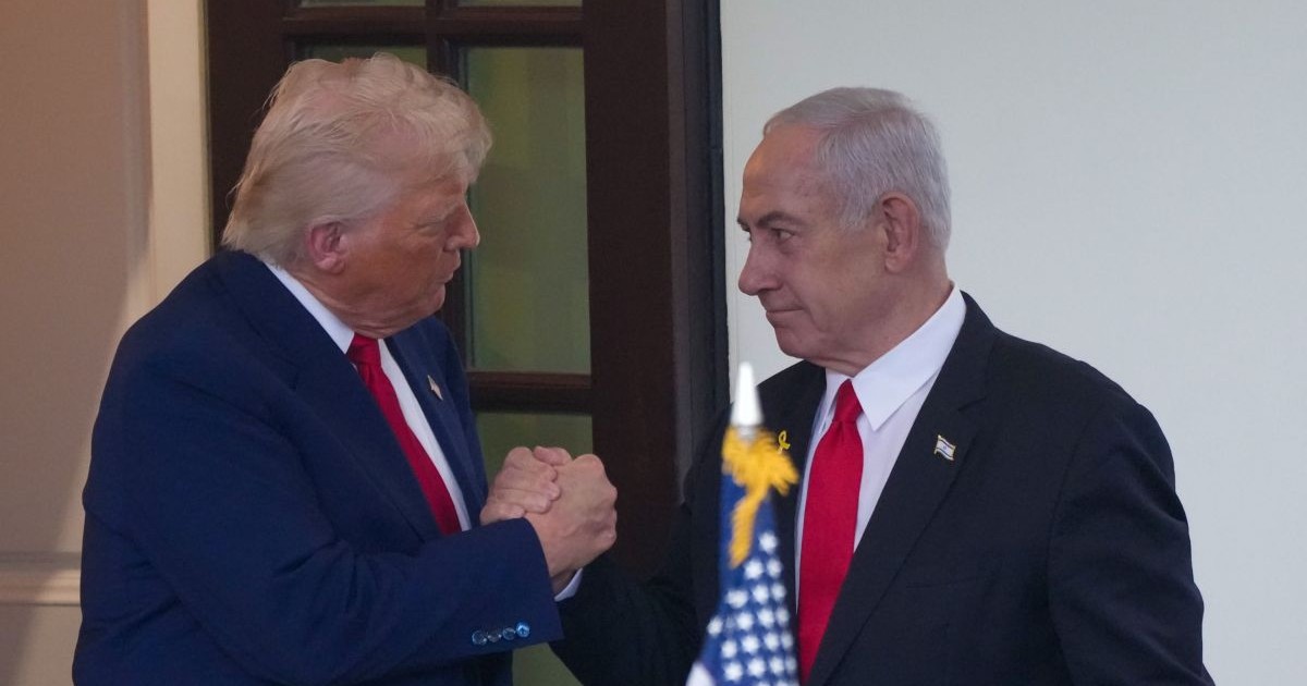 Donald Trump dă mâna cu Benjamin Netanyahu stând în picioare și având în față un steag american, aprilie 2025