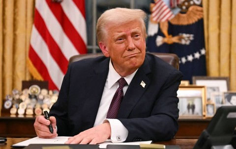 Donald Trump, îmbrăcat în costum, în timp ce stă la Biroul Oval, la Casa Albă, și semnează un document, în ianuarie 2025