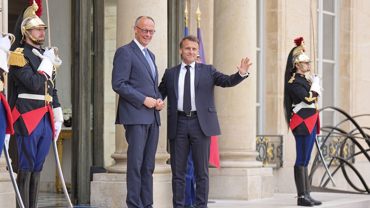 Președintele francez Emmanuel Macron âîl primește pe cancelarul german Friedrich Merz la pris. Cei doi dau mâna ș zîmbesc. Alături se află doi soldați din garda franceză