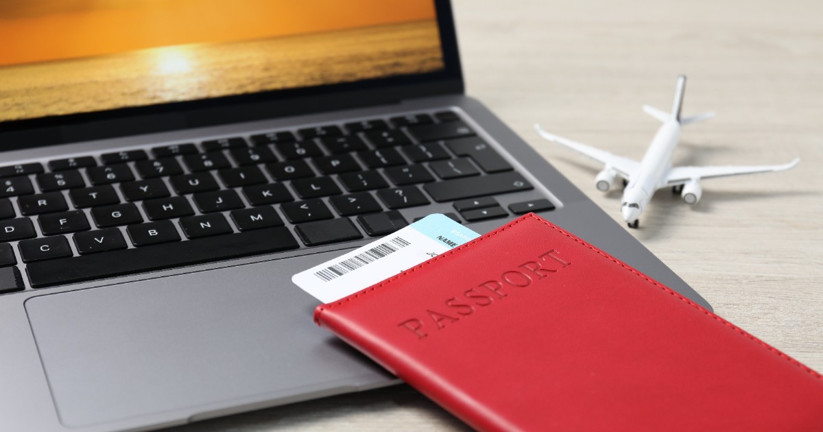 Un pașaport roșu așezat pe un laptop în care este un bilet de avion.