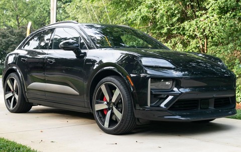 masina neagra suv marca Porsche parcata in curte cu fundal verde din plante, copaci