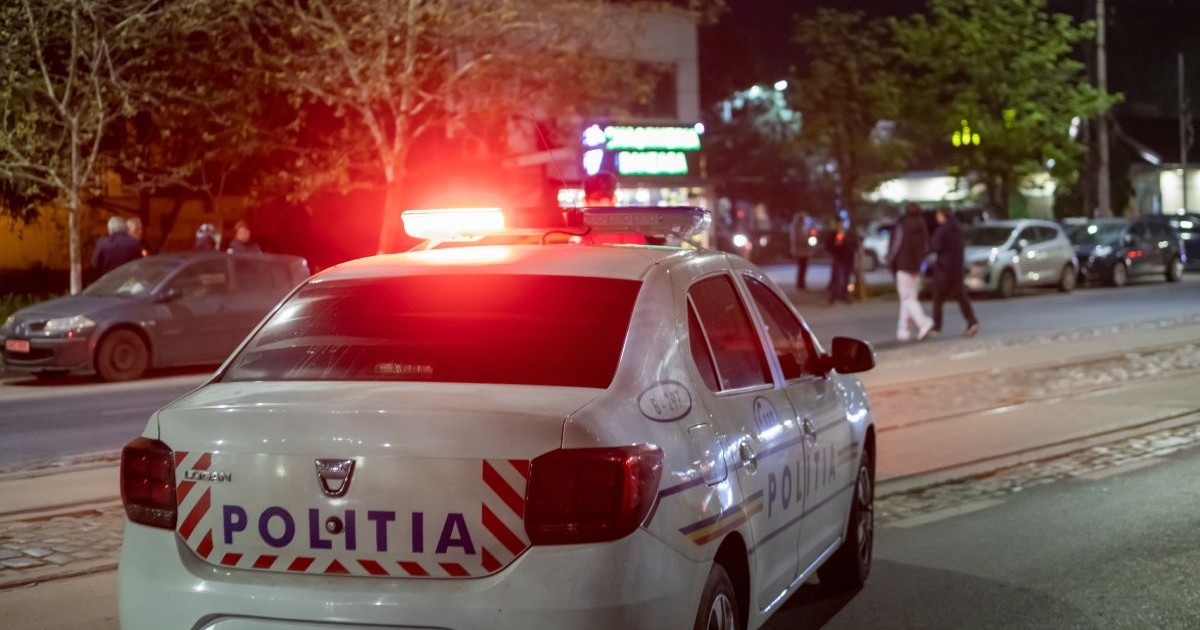 Mașină de Poliție, cu girofarul pornit, de culoare roșie, pe o stradă, pe timp de noapte
