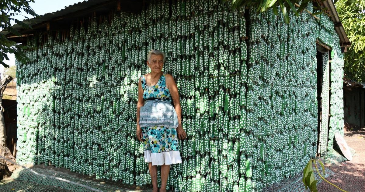 Maria Ponce, îmbrăcată cu o rochie albastră, în fața casei din sticle de plastic de culoare verde