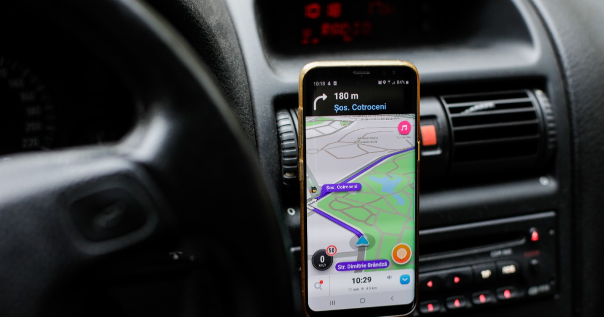 Imaginea prezintă un smartphone montat pe bordul unui automobil, rulând aplicația de navigație Waze ce afișează un traseu pe Șoseaua Cotroceni.