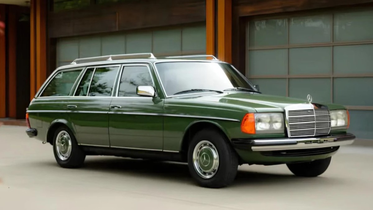 Imaginea prezintă un autoturism clasic Mercedes-Benz Break (W123) de culoare verde, parcat pe o alee din fața unei case moderne cu porți de garaj elegante.