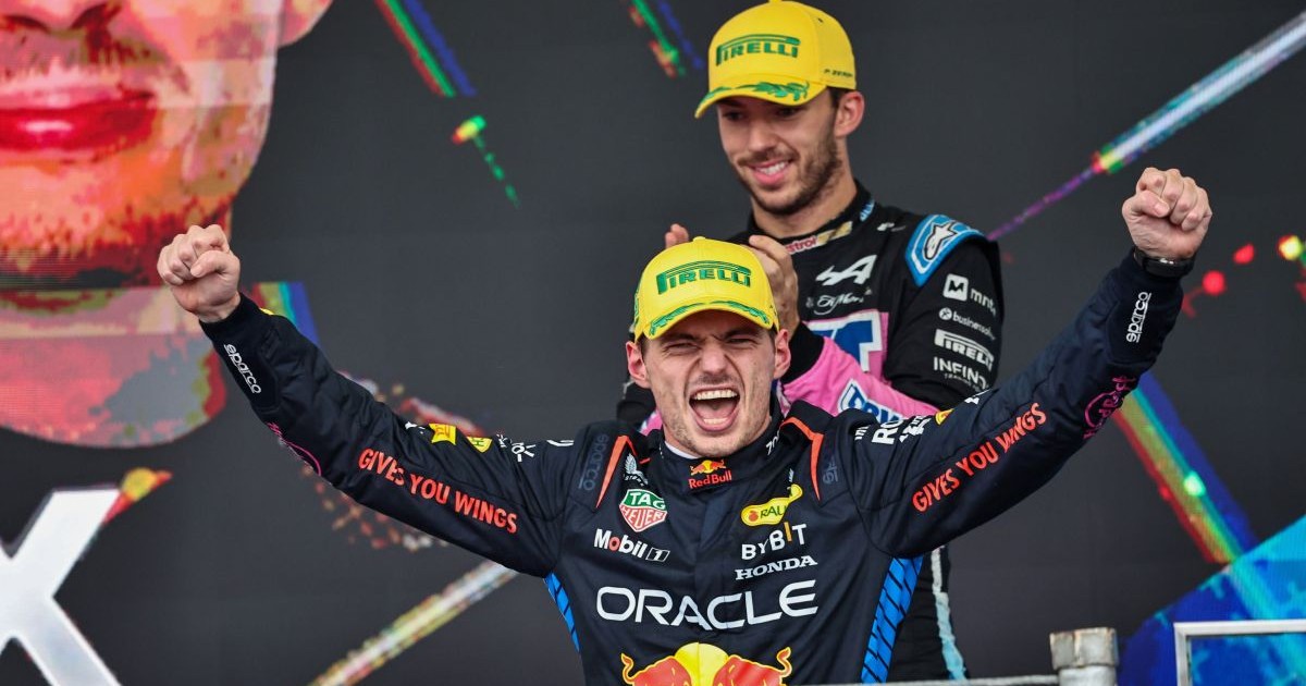 Max Verstappen, cu ambele mâini ridicate, sărbătorind victoria, îmbrăcat în costumul său de pilot de Formula 1