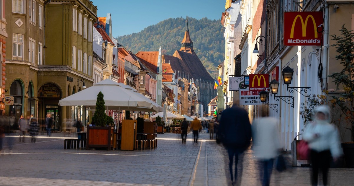 Imagine cu turiști care merg pe o stradă din centrul Brașovului. În fața se vede Biserica Neagră
