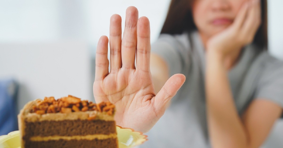 Ce înseamnă expresia „pune-ți pofta în cui” - Imagine cu o femeie care face un gest de refuz cu mâna pentru a refuza prăjitura care i se oferă