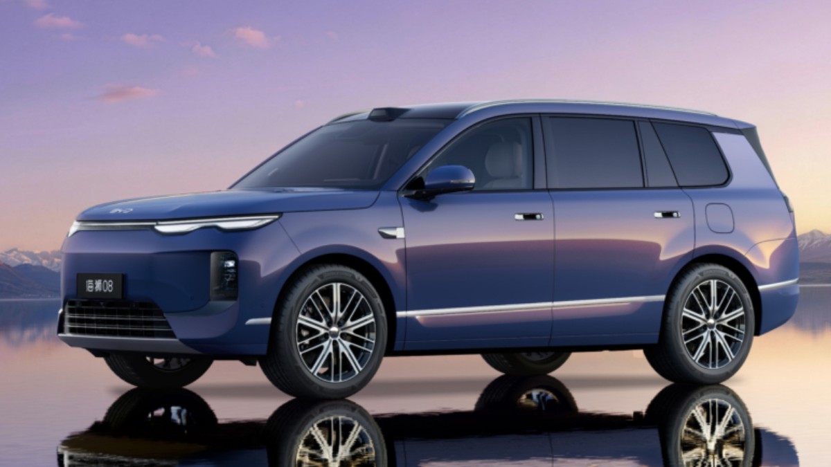 Un SUV de culoare albastră, marca BYD, se oglindește pe o suprafață lucioasă, având în fundal un peisaj montan la apus.