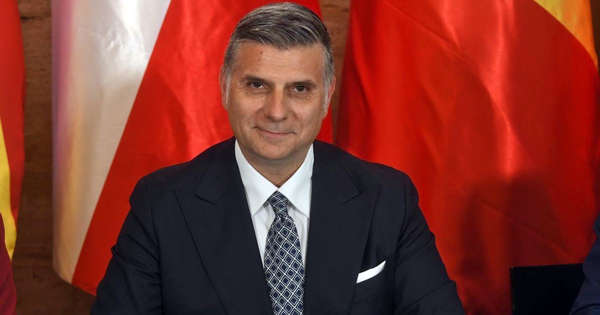 Un barbat in costum avand un fundal rosu in spate