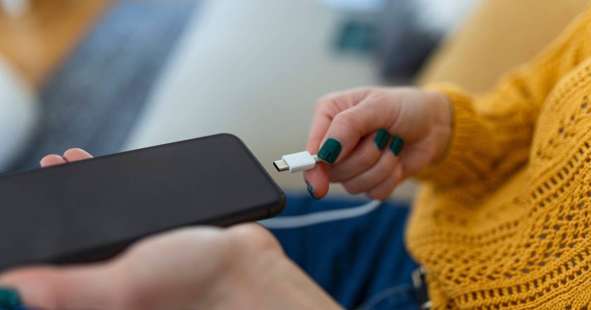 mainile unei femei care conecteaza cablul de incarcare in telefonul mobil