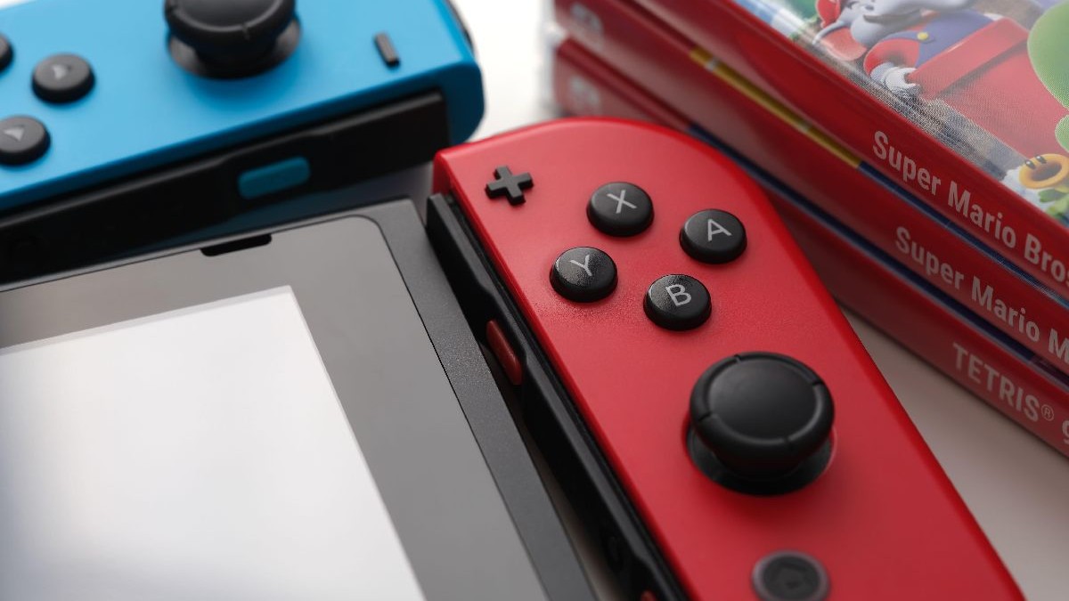 O consolă Nintendo Switch, cu un controller detașat, așezată lângă trei cutii de jocuri.