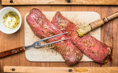 Raw meat fillets marinating with rub brush and fork on wooden background, top view