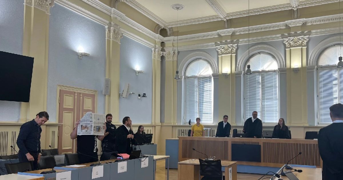 O sală de tribunal cu bărbați în robe și un alt bărbat care-și acoperă fața cu un ziar