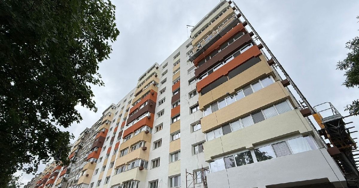 Imaginea surprinde un bloc cu mai multe etaje, cu balcoane vopsite în diferite nuanțe de bej, portocaliu și alb