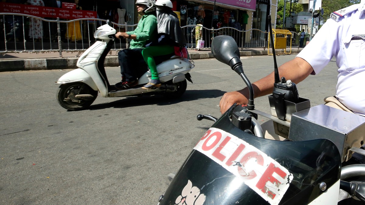 O fetiță din India a fost violată cu un furtun. Scuter de Poliție, în India, pe lângă care mai trece un al scuter, civil, cu doi pasageri