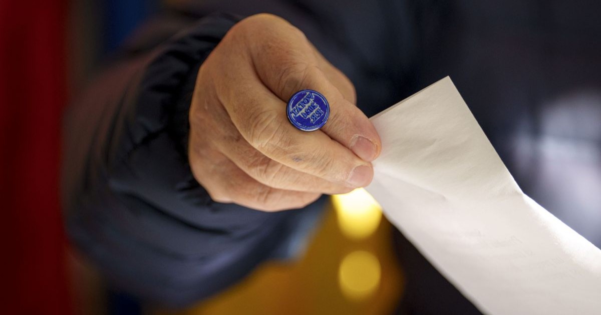 Imagine ilustrativă cu o mână de bărbat care ține o ștampilă de vot și un buletin de vot