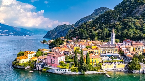 Imagine văzută de sus asupra orașului Varenna de pe malul Lacului Como din Italia, cu clădiri colorate și munți pe fundal.