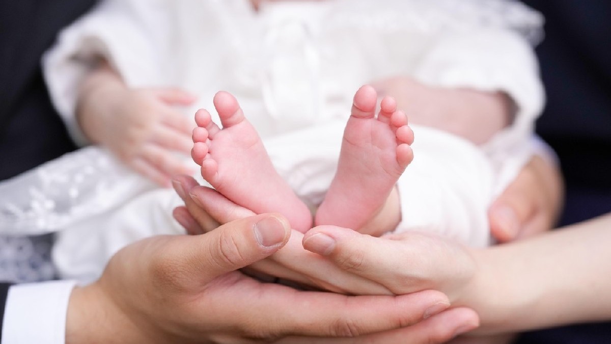 Un prim-plan arată picioarele mici ale unui bebeluș, ținute în mână de părinți
