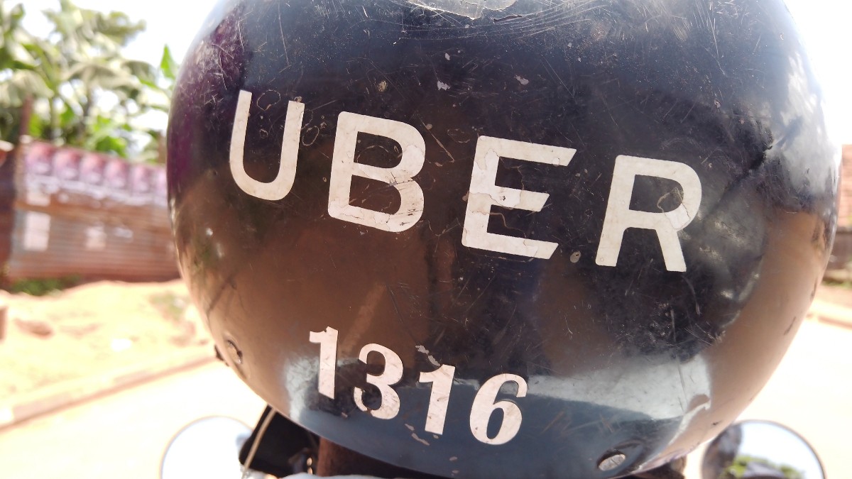 În imagine este prezentată partea din spate a unei căști negre de motocicletă, pe care sunt inscripționate cu alb textul „UBER” și numărul „1316”.